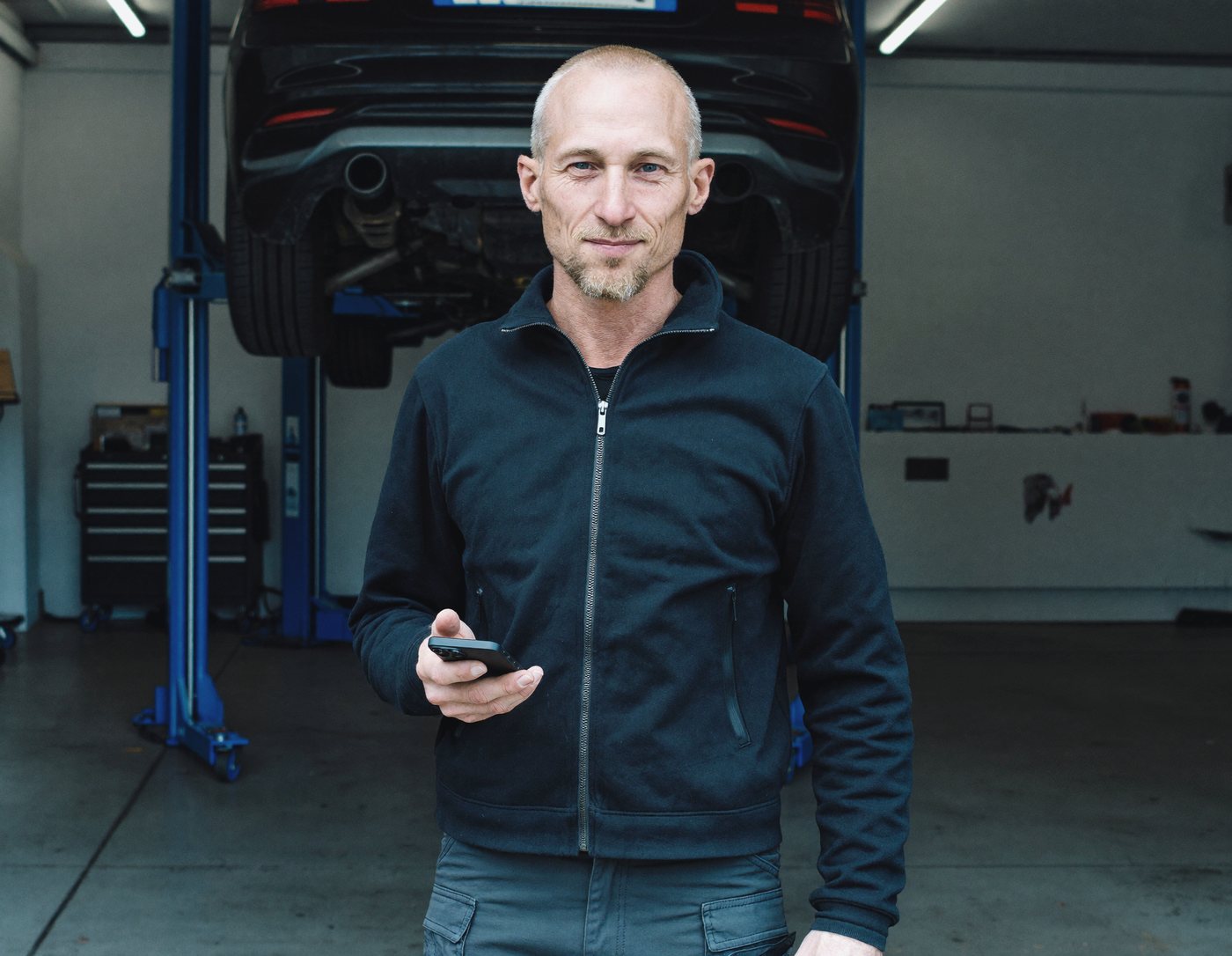 Rick staat in zijn werkplaats met zijn telefoon in de hand